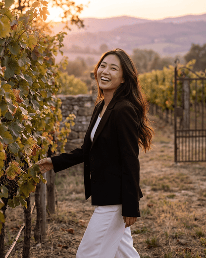 A woman wearing a black Celeste Blazer by Slimona, smiling in a vineyard during sunset.