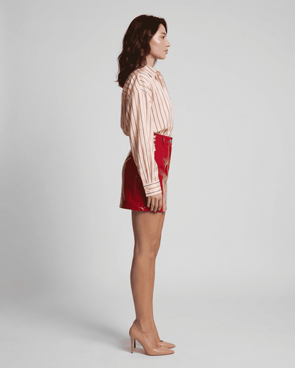 Side view of a model wearing a high-waisted Crimson Mini Skirt by Slimona, featuring a striking red glossy finish.