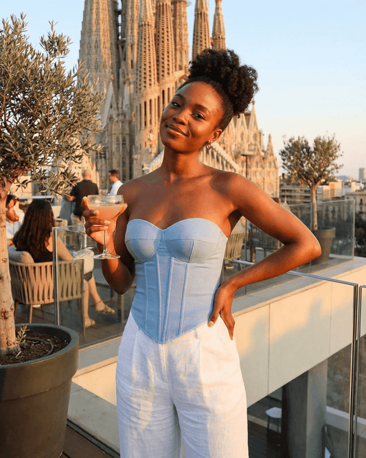 Denali Corset Top by Slimona, a faux denim cup bustier worn by a woman enjoying a cocktail with a city view.