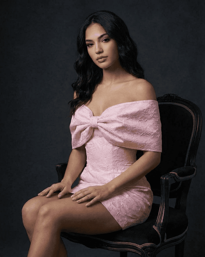 Model showcasing the Fiora Mini Dress by Slimona with bowknot off-the-shoulder detail in soft pink.