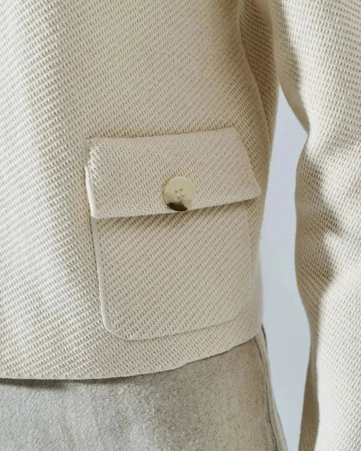 Close-up of the Lazio Cropped Jacket by Slimona showcasing the pocket and button detail in cream fabric.