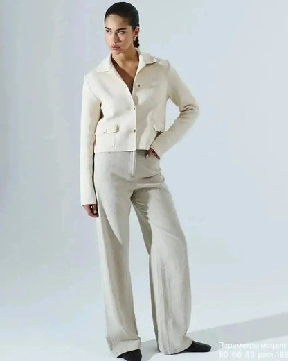 Model wearing the Lazio Cropped Jacket by Slimona, showcasing an elegant cream color with button closure, paired with light trousers.