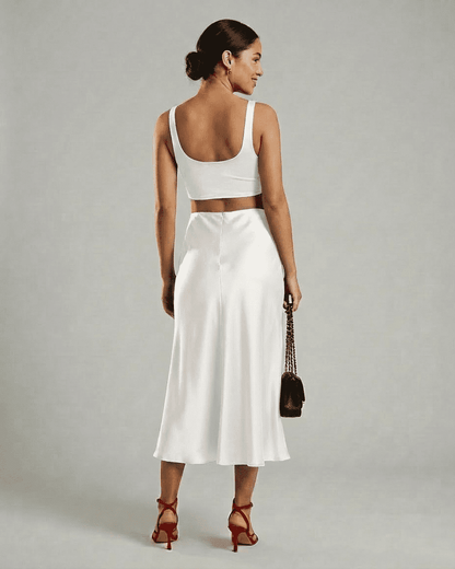 Woman in white back view wearing Slimona Luna Midi Skirt and cropped top, showcasing elegant satin mermaid design.