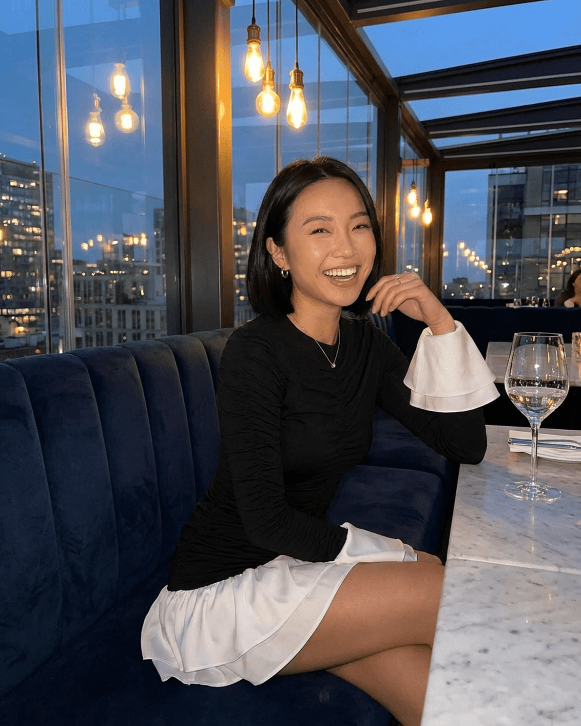 Luna Mini Dress worn by a smiling woman in a chic setting, showcasing its elegant style and flared sleeves.