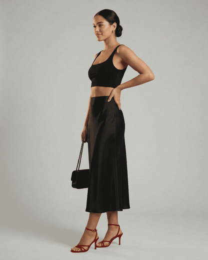 Model wearing Slimona Noirelle Midi Skirt, a sleek satin mermaid midi skirt, styled with a black top and red heels.