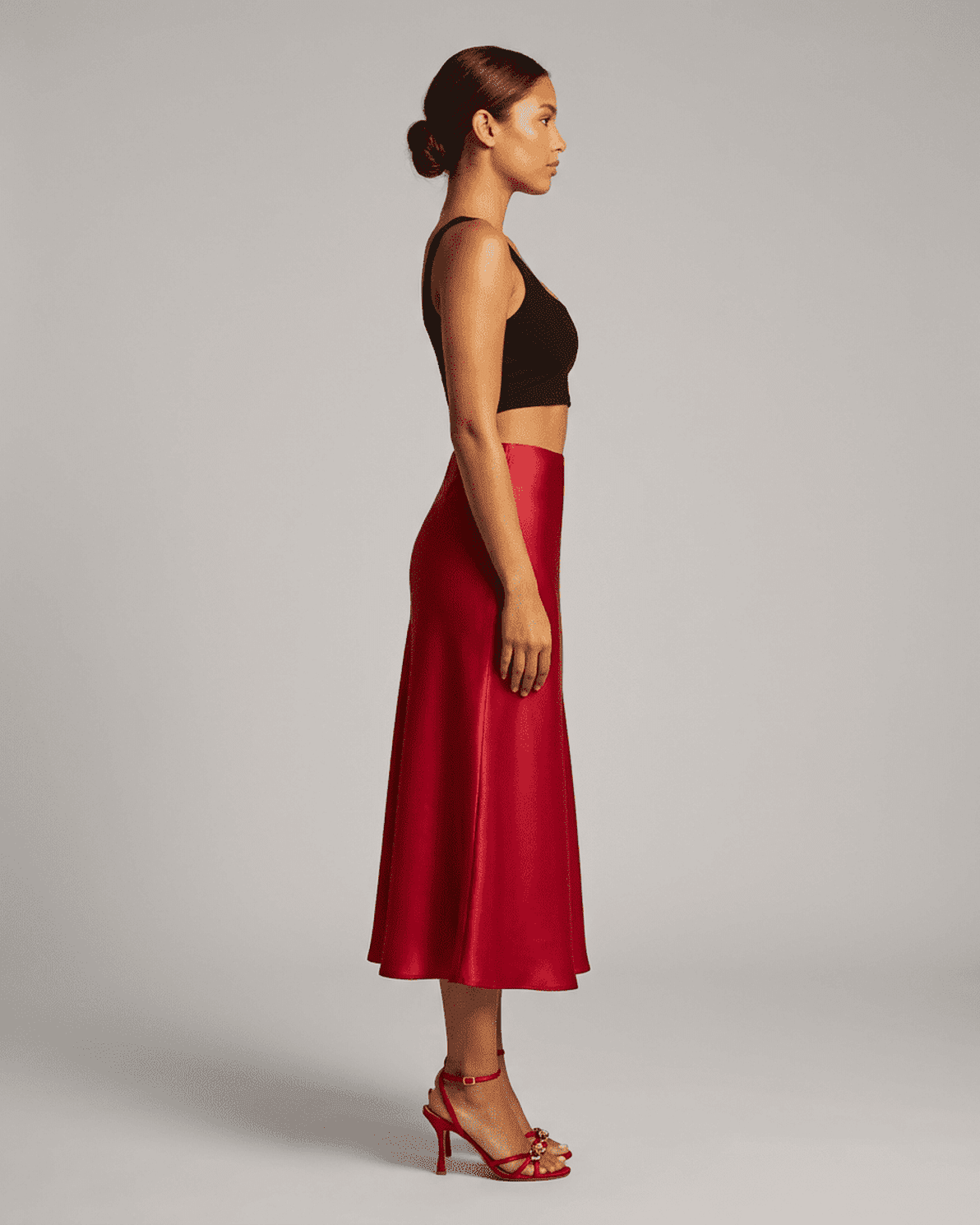 Side view of a woman wearing the Rosalia Midi Skirt by Slimona in rich red satin, showcasing its elegant silhouette.