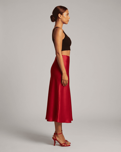 Side view of a woman wearing the Rosalia Midi Skirt by Slimona in rich red satin, showcasing its elegant silhouette.