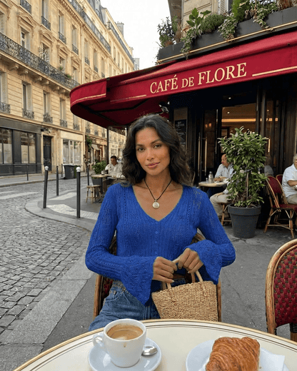 A woman wearing the Royal Cardigan sits at Café de Flore in Paris, enjoying coffee and a pastry.
