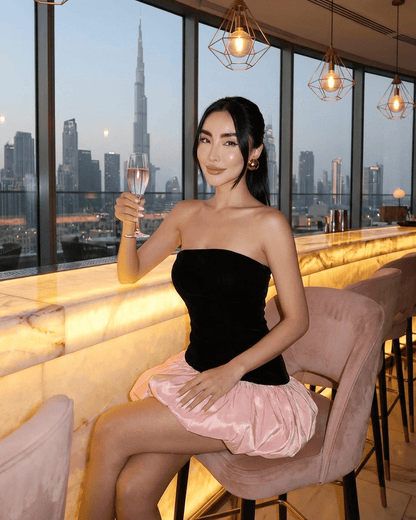 Selina Mini Dress by Slimona, featuring a strapless black velvet top and a playful pink puff skirt, against a city skyline.