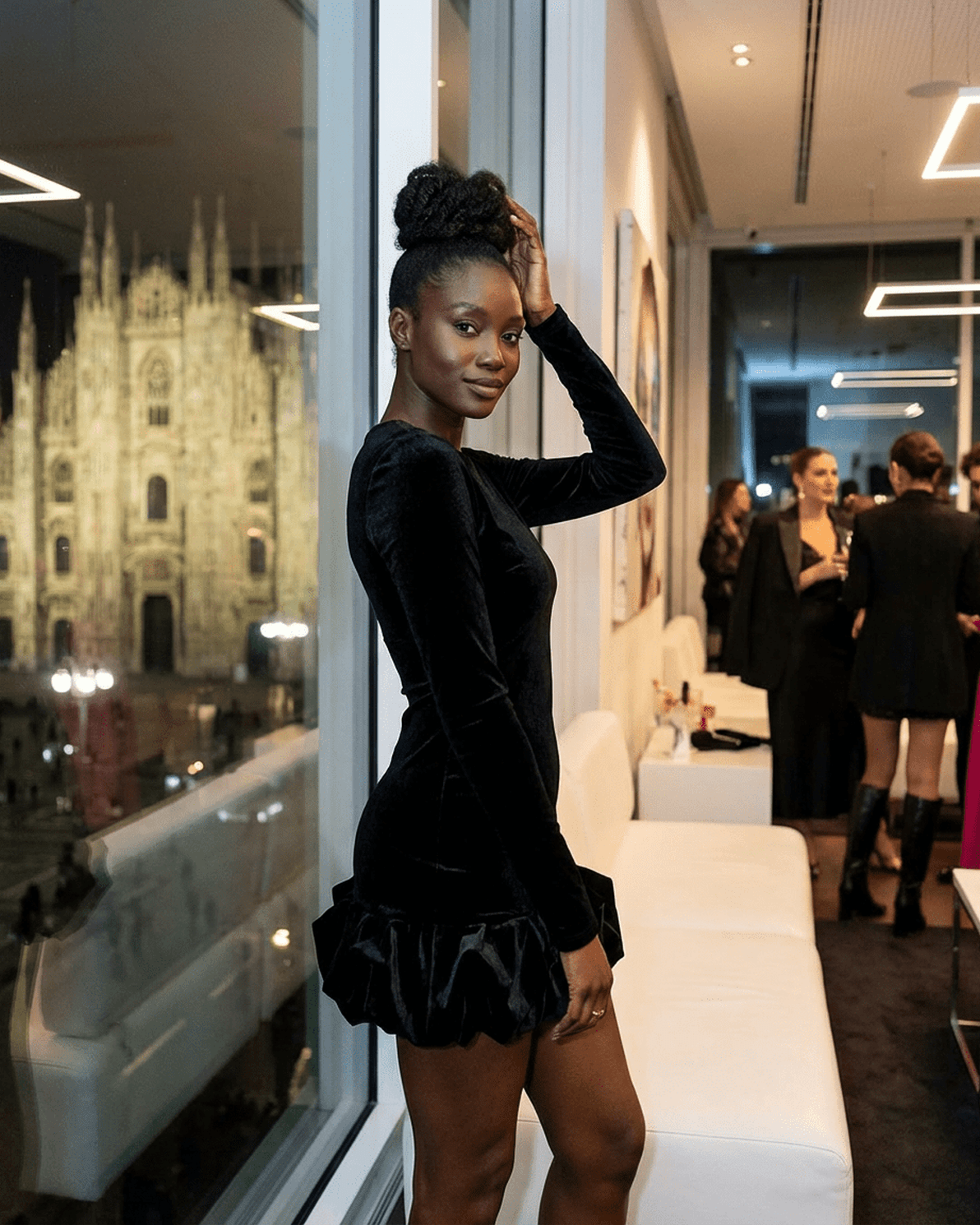 Model showcasing Velora Mini dress by Slimona, featuring luxe black velvet and pleated hem, in a stylish indoor setting.