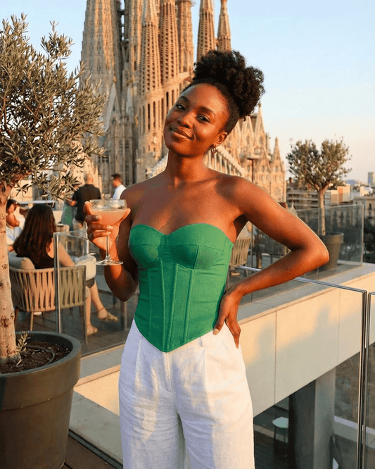 Woman wearing Verde Corset Top by Slimona, holding a cocktail with a city view backdrop.