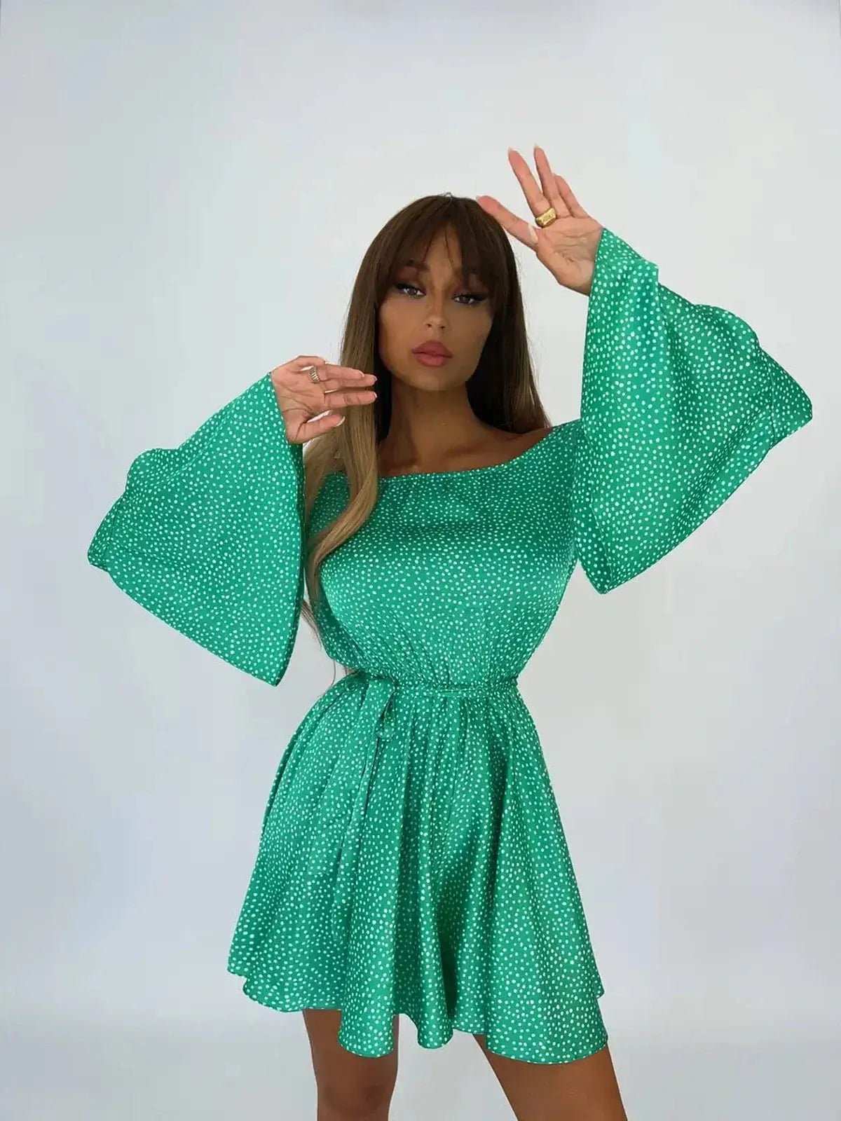 Model showcasing the Luna Dot Mini Dress, an off-shoulder green and white polka dot mini dress with flared sleeves.