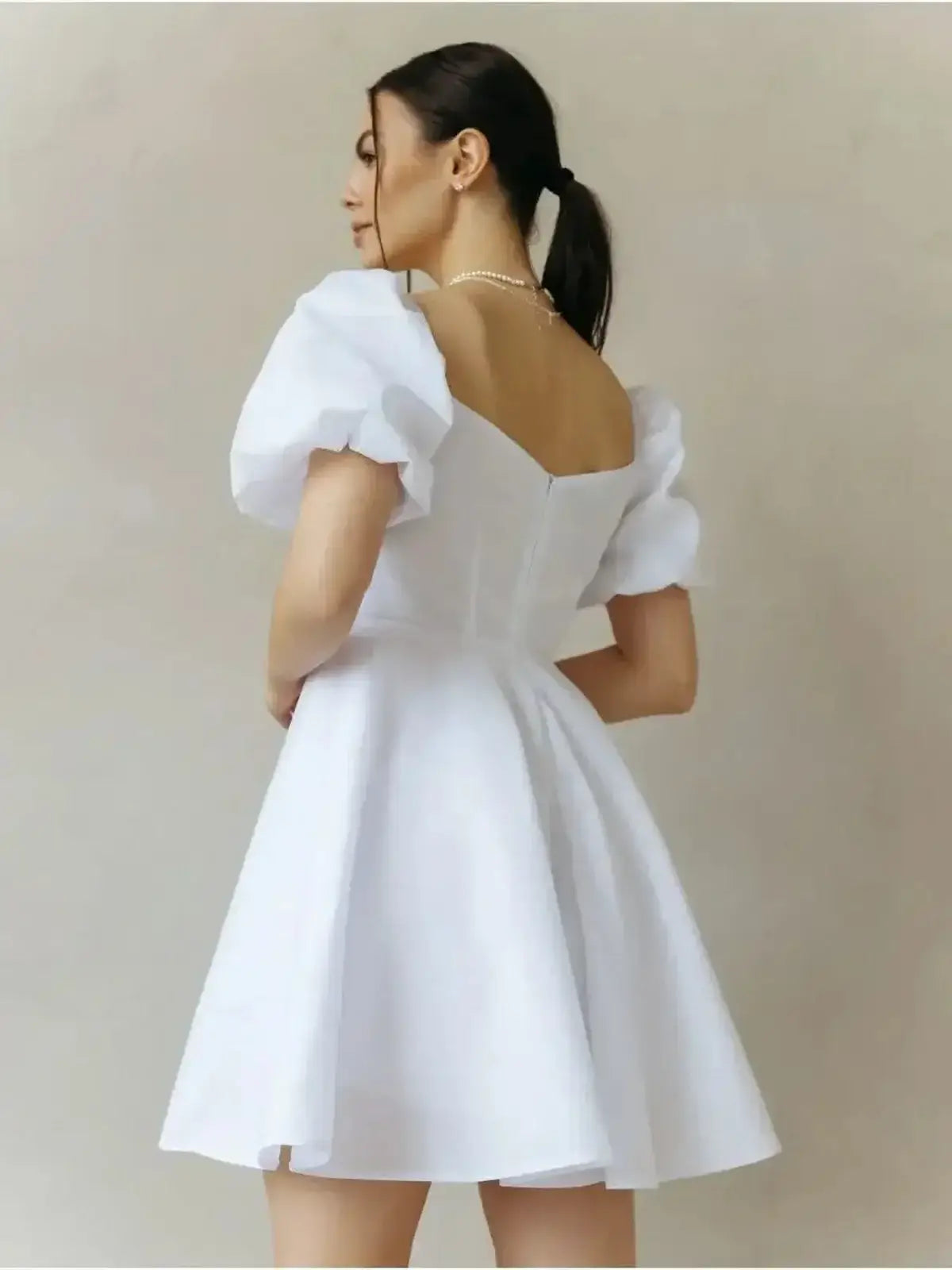 Woman wearing the Luna Pearl Mini Dress, a white cotton dress with puff sleeves and a flared skirt, perfect for summer occasions.