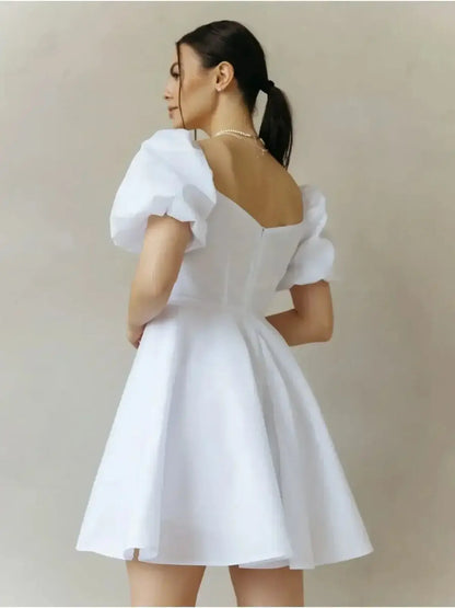 Woman wearing the Luna Pearl Mini Dress, a white cotton dress with puff sleeves and a flared skirt, perfect for summer occasions.