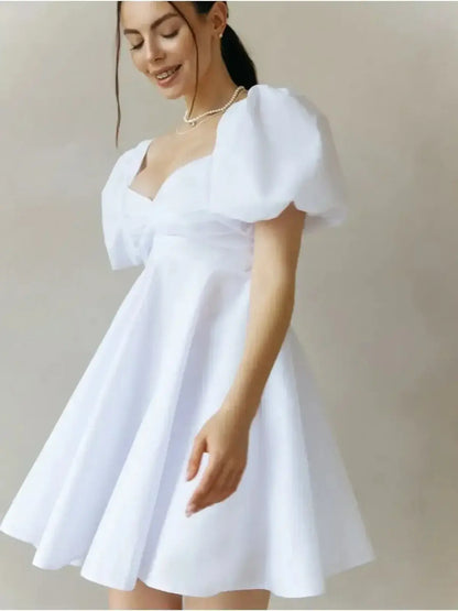 Model wearing the Luna Pearl Mini Dress, a white summer dress with puff sleeves and a sweetheart neckline.