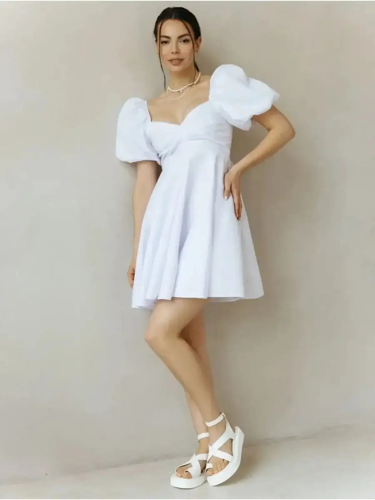 Model showcasing the Luna Pearl Mini Dress, a white summer dress with puff sleeves and a flared skirt.