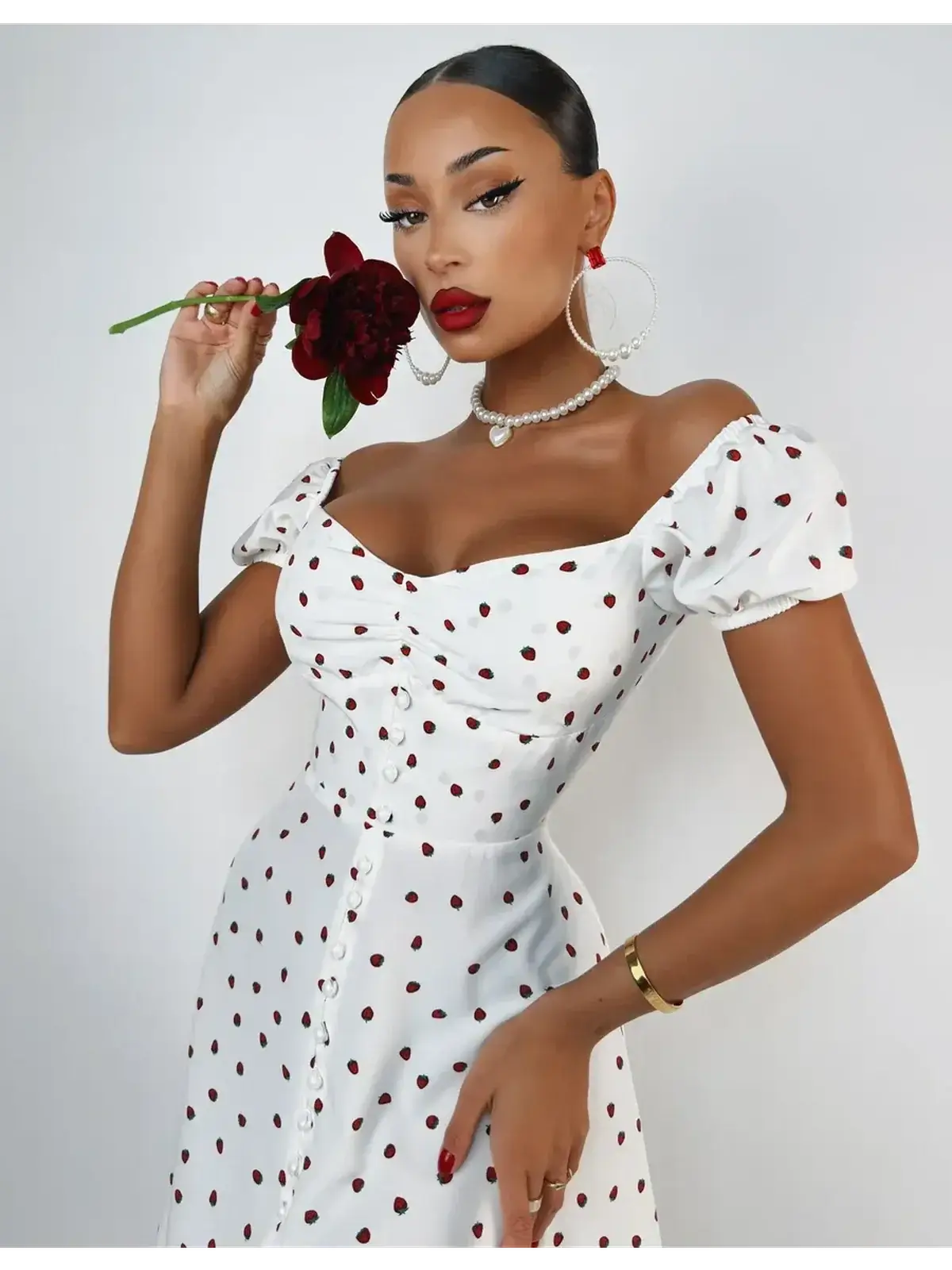 Woman in a white polka dot mini dress with puff sleeves holding a flower, showcasing a chic summer style.