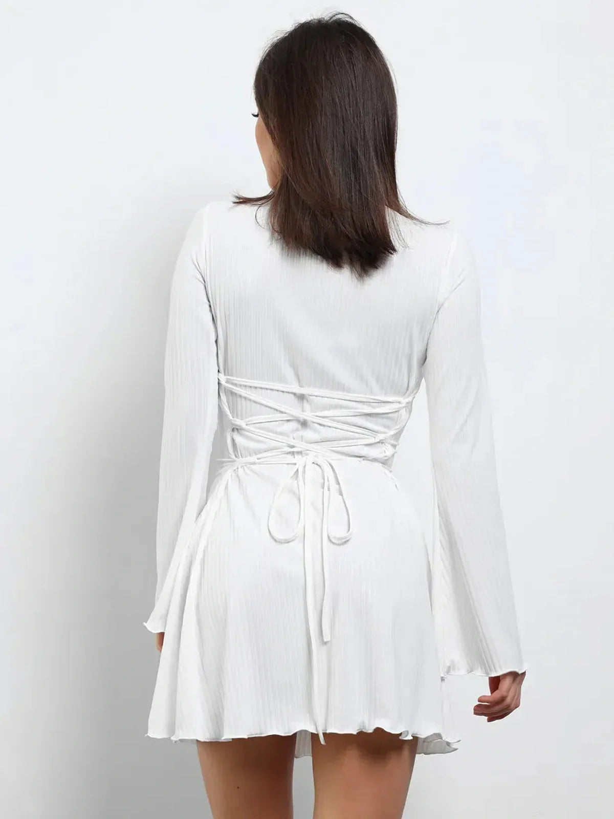 Back view of a woman in a white mini dress with lace-up design and flared sleeves, perfect for summer and wedding guest wear.