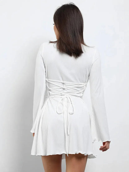 Back view of a woman in a white mini dress with lace-up design and flared sleeves, perfect for summer and wedding guest wear.