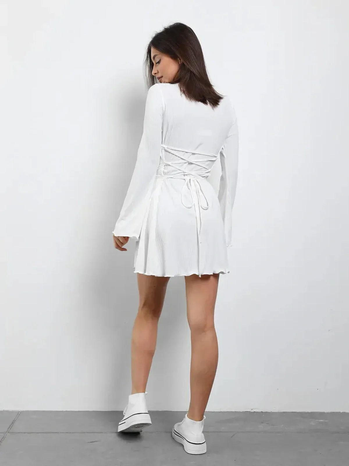 Back view of a woman in a white lace-up mini dress, perfect for summer and wedding guest occasions.