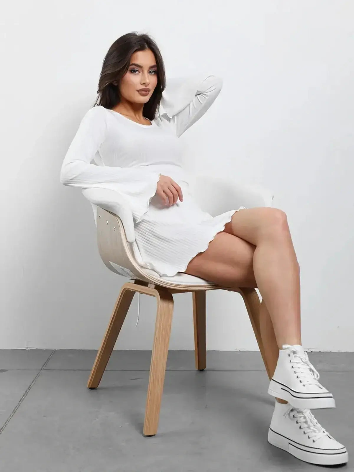 Model wearing a white Luxe Lace-Up mini dress with flared sleeves, seated in a chair, showcasing a modern and elegant style.