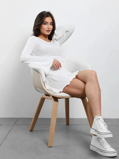 Model wearing a white Luxe Lace-Up mini dress with flared sleeves, seated in a chair, showcasing a modern and elegant style.