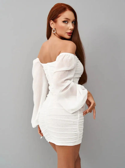 Model showcasing a Luxe Spark white mini dress with off-the-shoulder neckline and ruched bodice, perfect for weddings or parties.