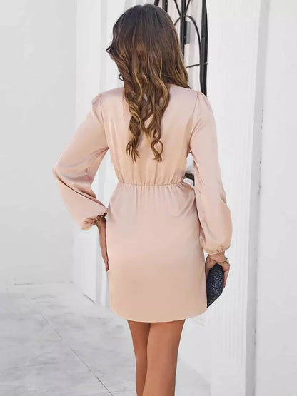Back view of a woman wearing a blush mini wrap dress with long sleeves and a cinched waist, ideal for summer occasions.
