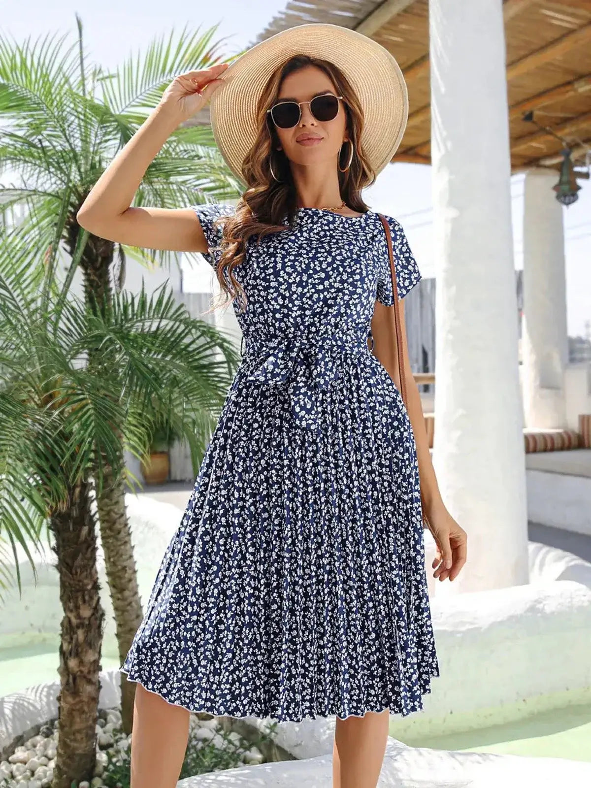 Model wearing a floral midi dress with a cinched waist and cap sleeves, complemented by a sun hat and sunglasses.
