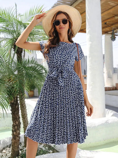 Model wearing a floral midi dress with a cinched waist and cap sleeves, complemented by a sun hat and sunglasses.
