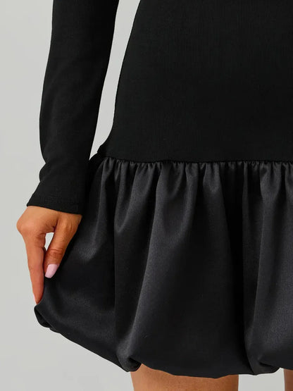 Close-up of a black mini dress with an off-the-shoulder neckline and a balloon skirt, showcasing modern elegance.
