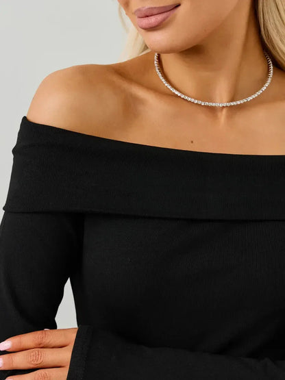 Close-up of a woman wearing an off-the-shoulder black dress with a pearl necklace, showcasing modern elegance.