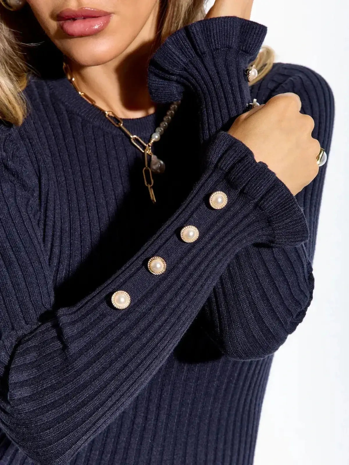 Close-up of a woman's navy ribbed dress showcasing pearl button details on long sleeves.