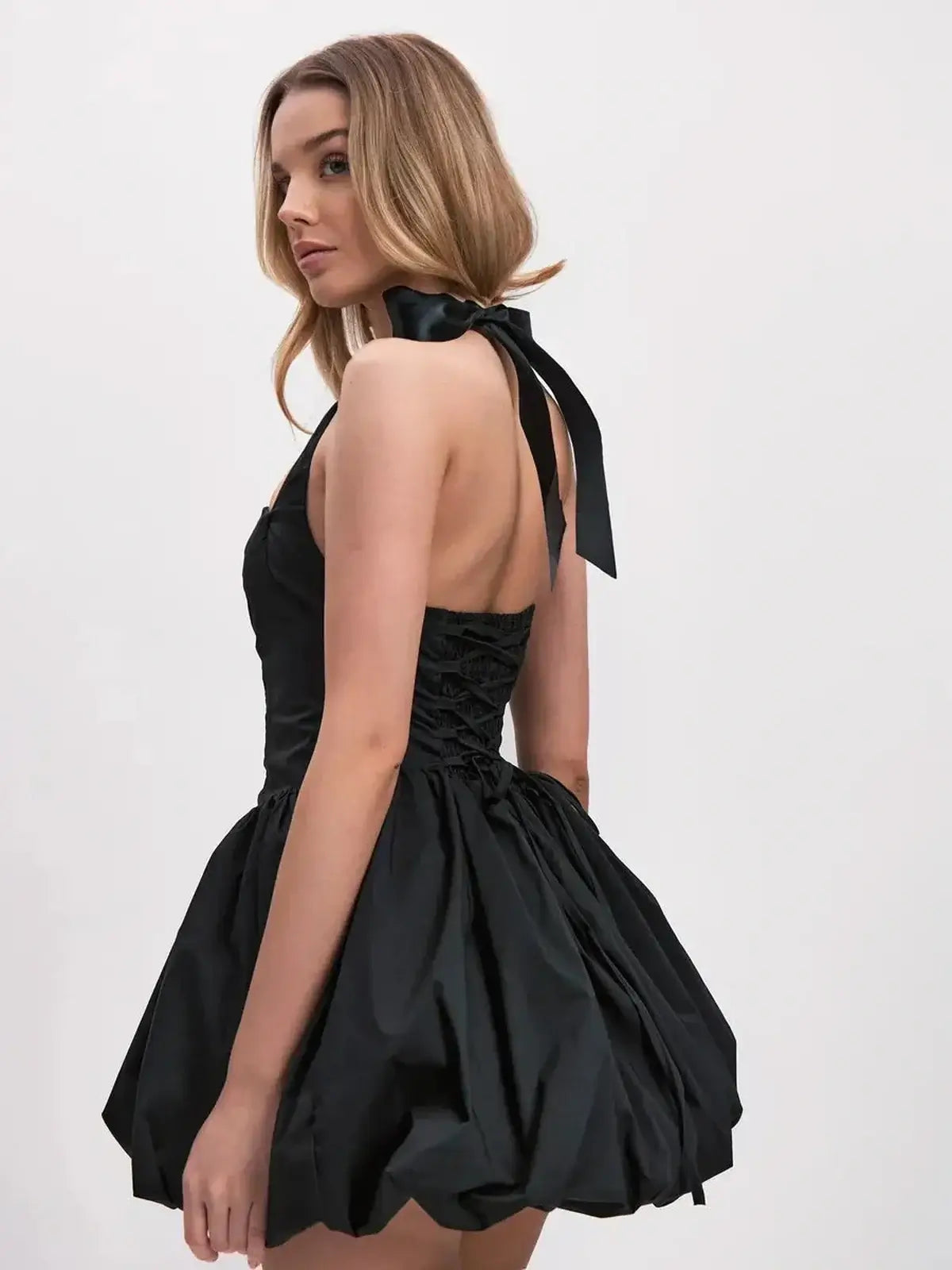 Model wearing a bold black mini dress with voluminous bubble skirt and halter straps, showcasing a modern silhouette.