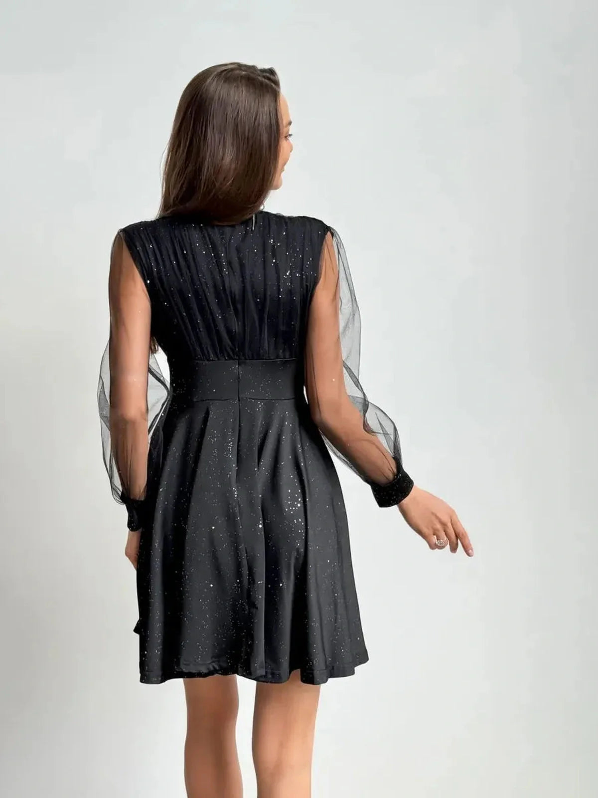 Back view of the black mini dress with sheer long sleeves and shimmering fabric, perfect for party and evening occasions.