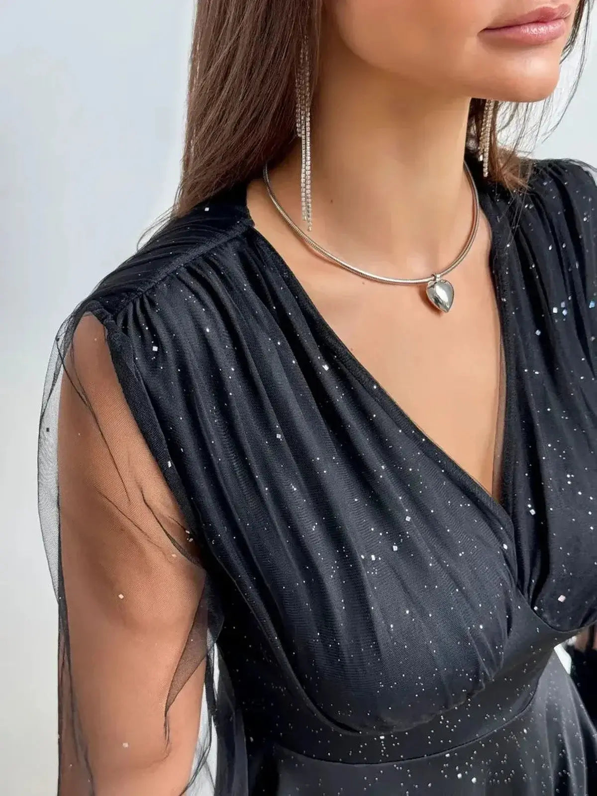 Close-up of the elegant Midnight Spark black mini dress featuring a plunging neckline and shimmering fabric with sheer sleeves.