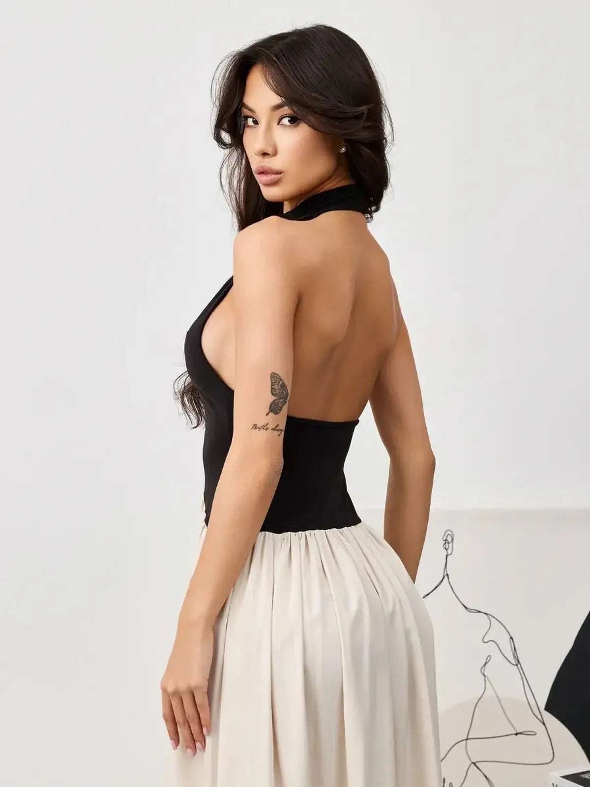 Model wearing the Muse Hourglass midi dress, featuring a sleek black halter bodice and flowing beige skirt.