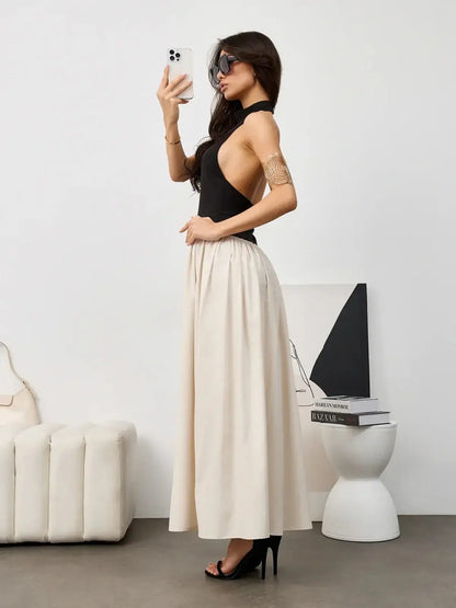 Model showcasing Muse Hourglass, a black halter dress with a beige maxi skirt, perfect for formal events and summer occasions.