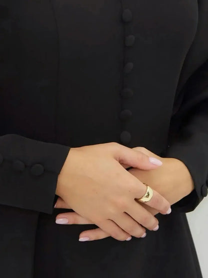 Close-up of hands wearing a gold ring, showcasing the button detail of the Noir Aura Mini Dress.