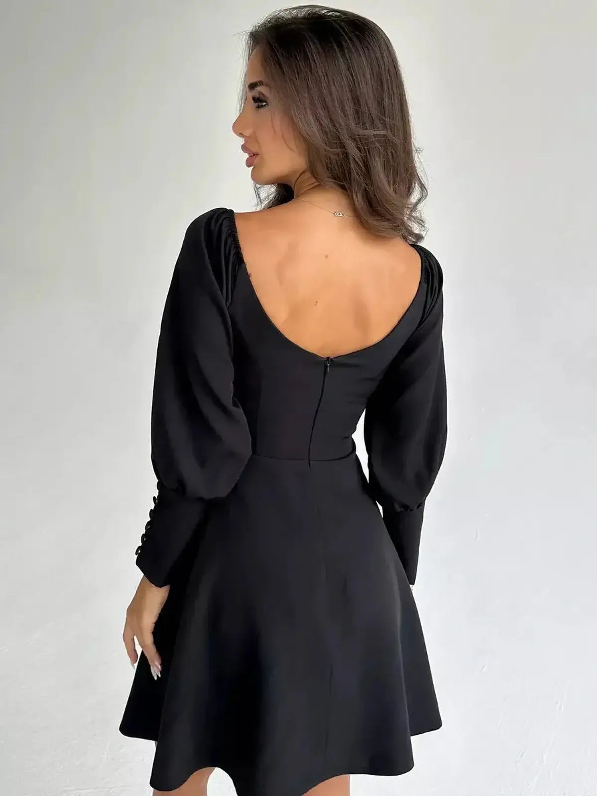 Back view of a model wearing a black mini dress with voluminous sleeves, showcasing a trendy and elegant style.