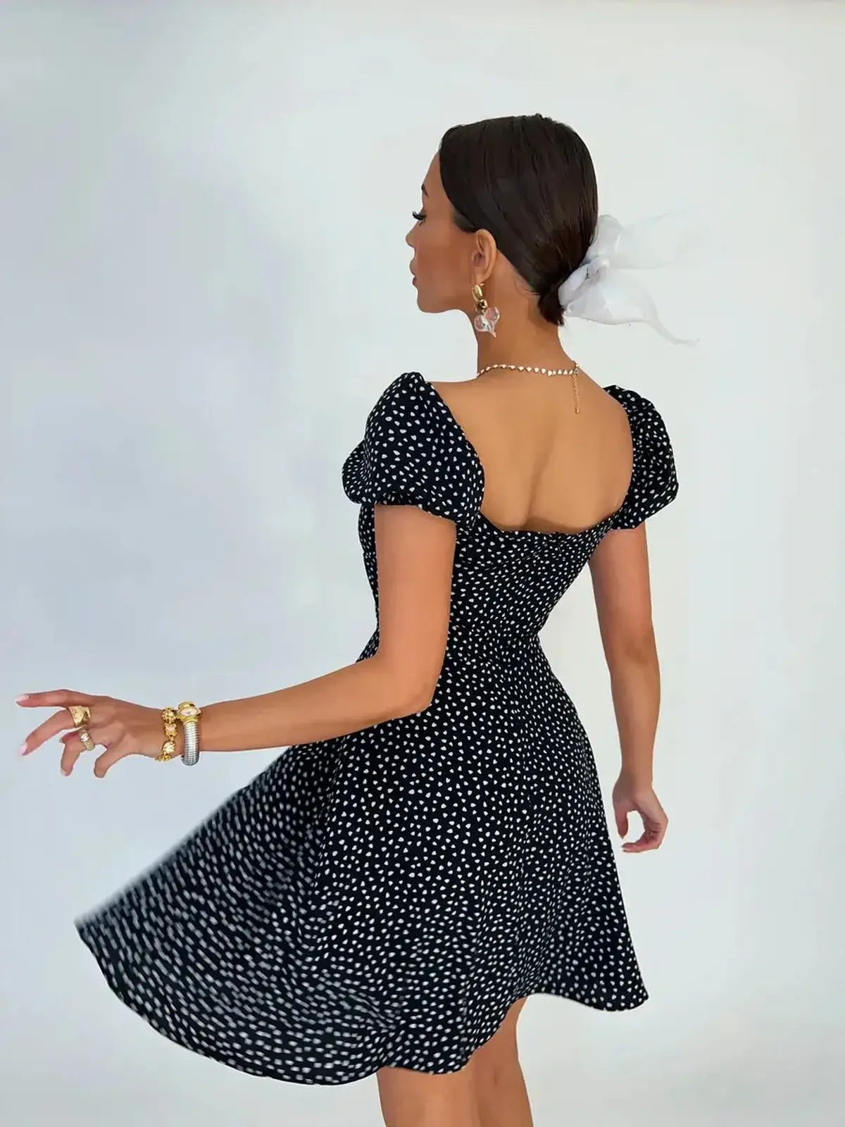 Model twirling in a Noir Chic Mini Dress featuring a black fabric with white dots, perfect for summer and evening occasions.