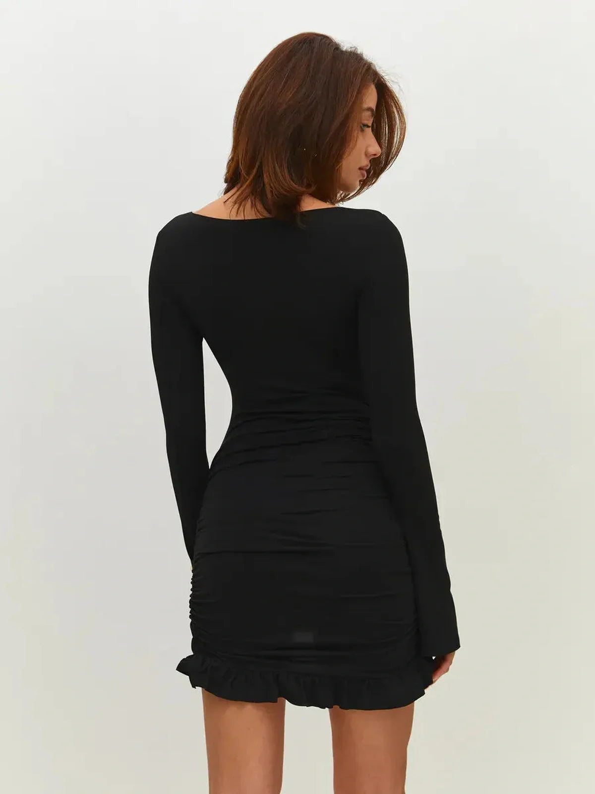 Back view of a woman wearing a black curve mini dress with long sleeves and ruffled hem, ideal for evening wear.