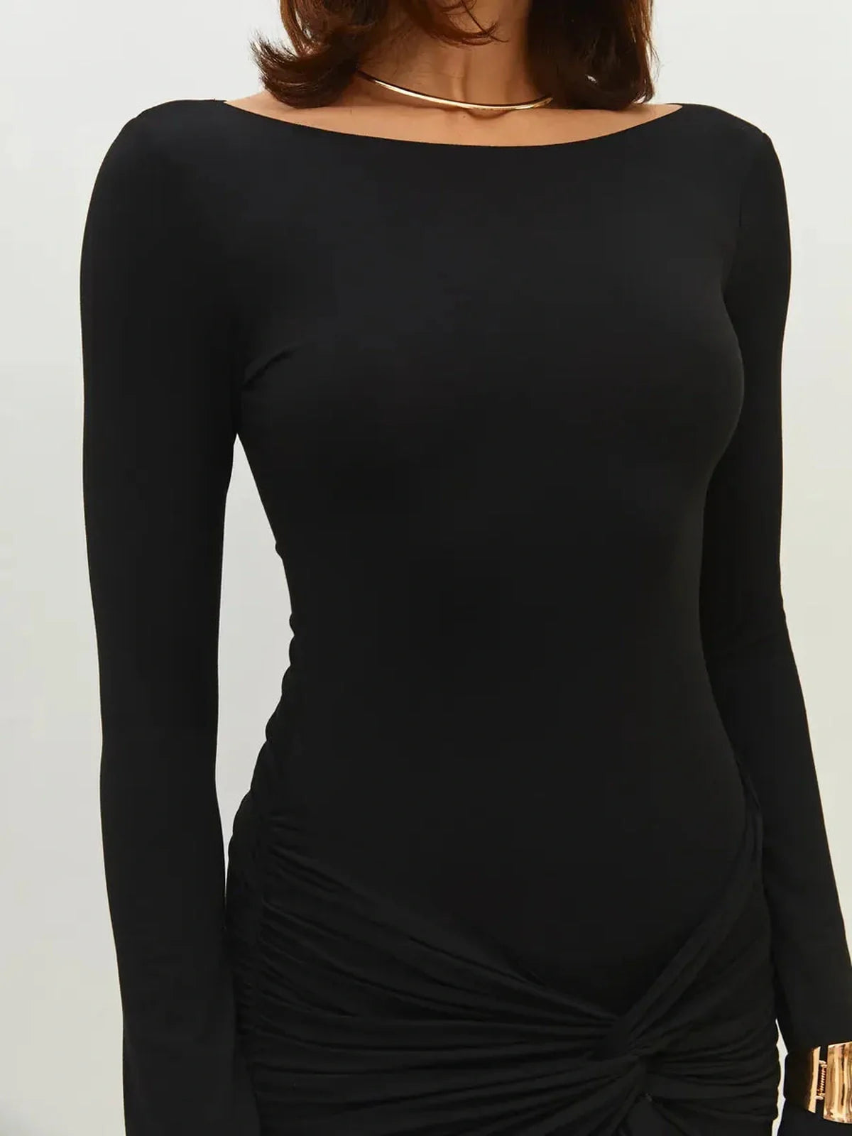 Close-up of woman wearing a sleek black mini dress with long sleeves and ruched skirt details.