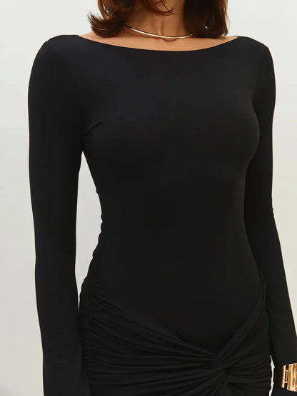 Close-up of woman wearing a sleek black mini dress with long sleeves and ruched skirt details.