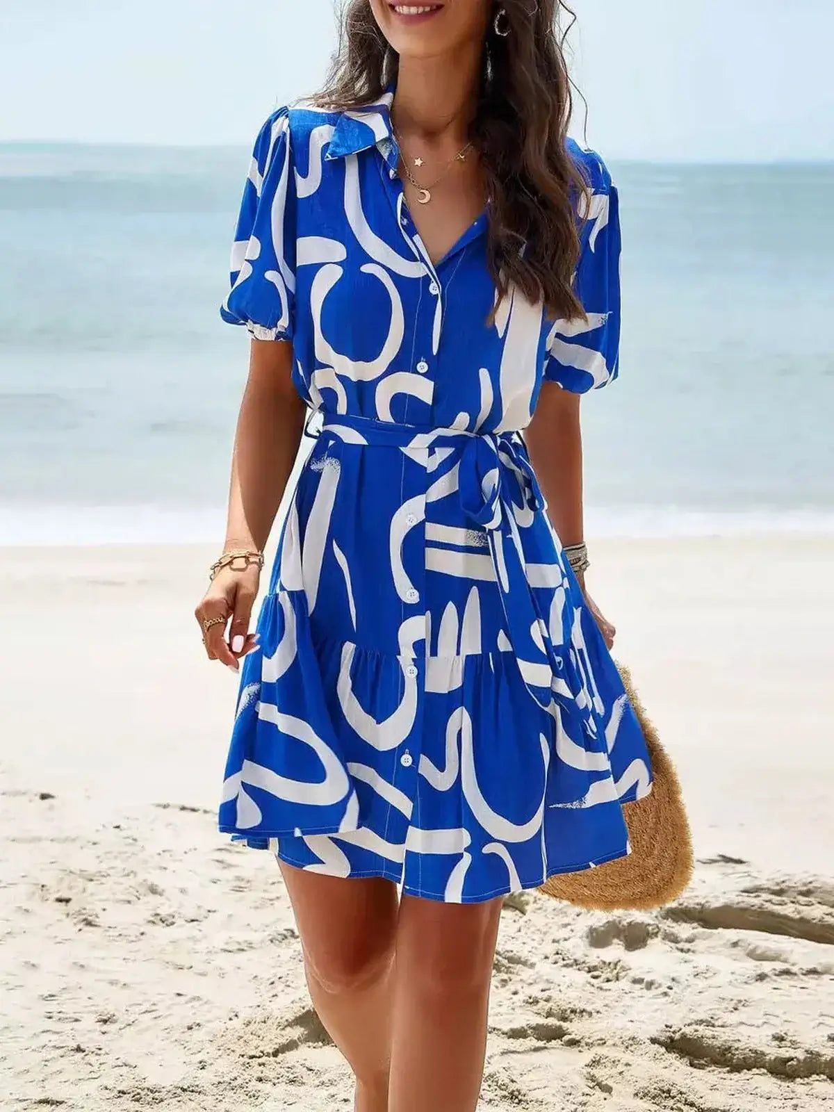 Woman in a blue-and-white abstract shirt mini dress at the beach, showcasing a stylish summer look.