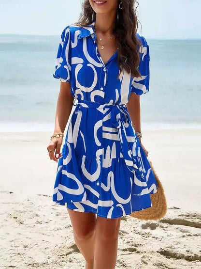 Woman in a blue-and-white abstract shirt mini dress at the beach, showcasing a stylish summer look.
