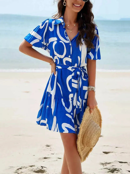 Woman wearing the Ocean Script Mini Dress in blue abstract pattern at the beach, perfect summer attire for outdoor events.