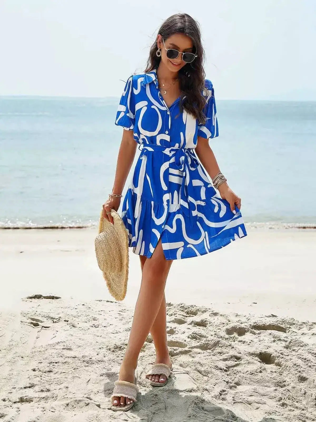Model wearing a blue-and-white Ocean Script Mini Dress at the beach, perfect for summer, weddings, and casual outings.