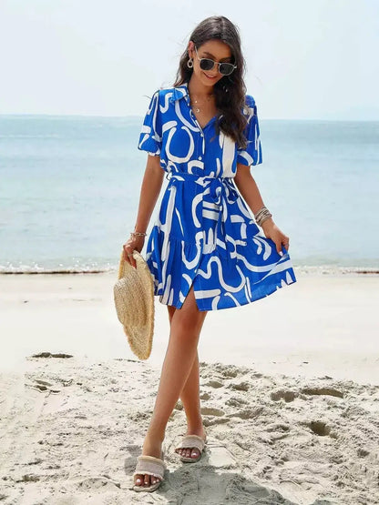 Model wearing a blue-and-white Ocean Script Mini Dress at the beach, perfect for summer, weddings, and casual outings.