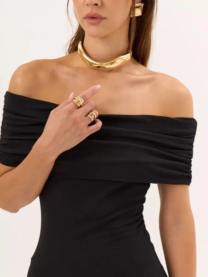 Model showcasing a black off-shoulder bodycon dress with ruched detailing, accessorized with a gold choker and rings.